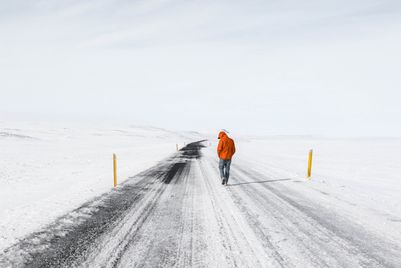 man-wearing-orange-jacket-walking-along-snowy-highway-road.jpg
